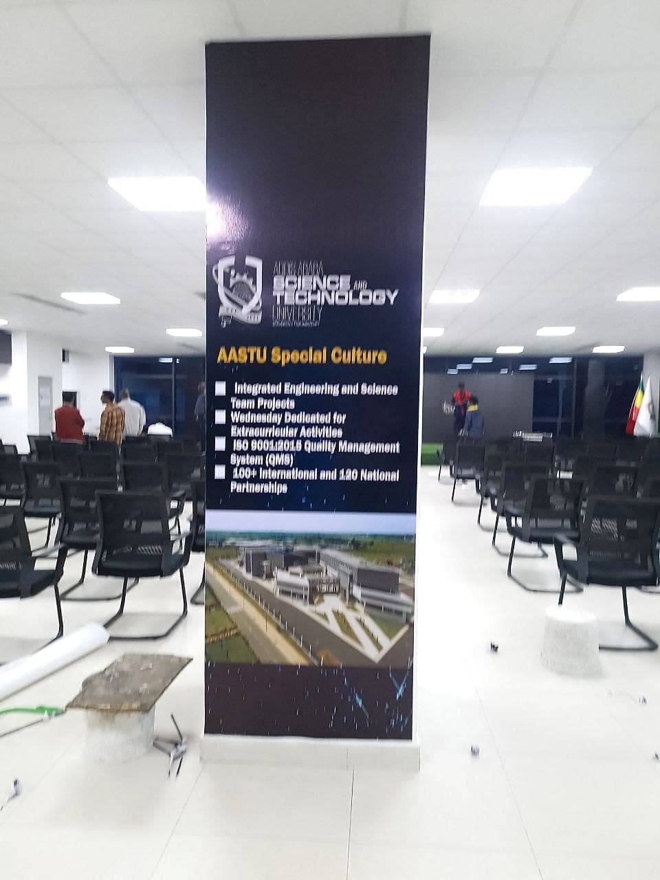 Dark AASTU roll-up banner listing university programmes, standing in a hall being set up
