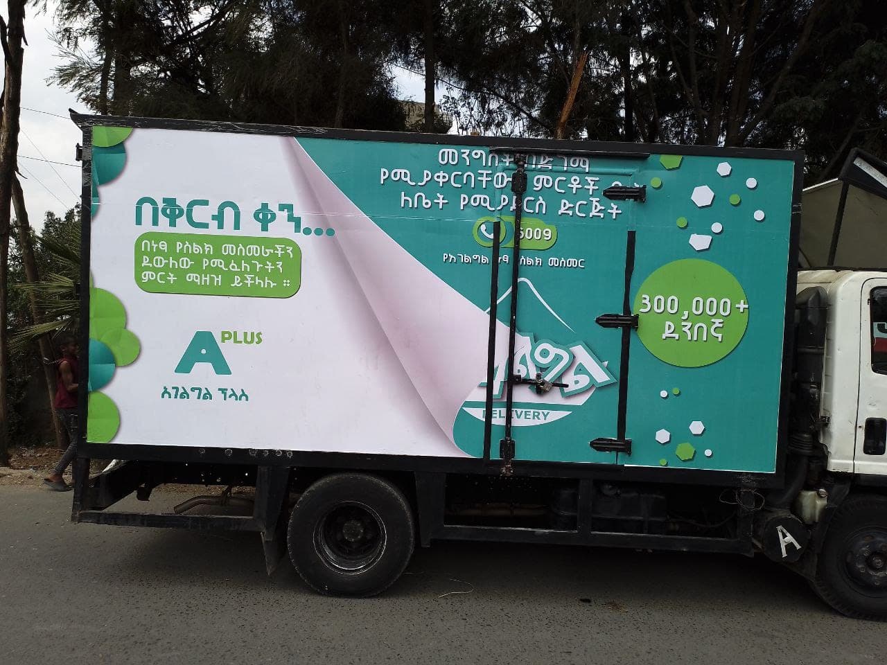 Green and white box truck printed with the Agelgil Delivery A Plus campaign and a peeling-page graphic device