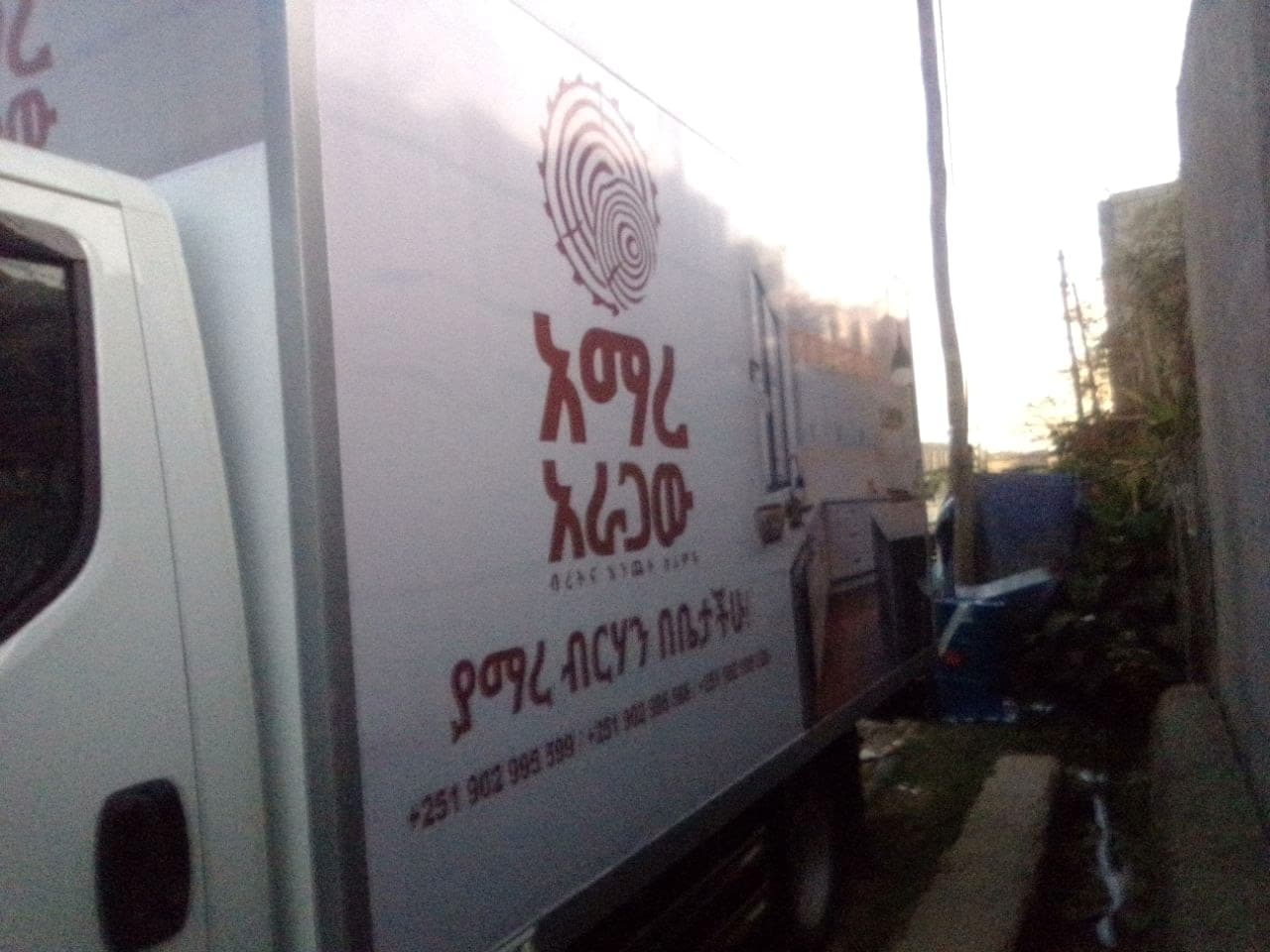 Side of the Amare Aragaw box truck against the evening sky, the logo and Amharic strapline running the length of the panel