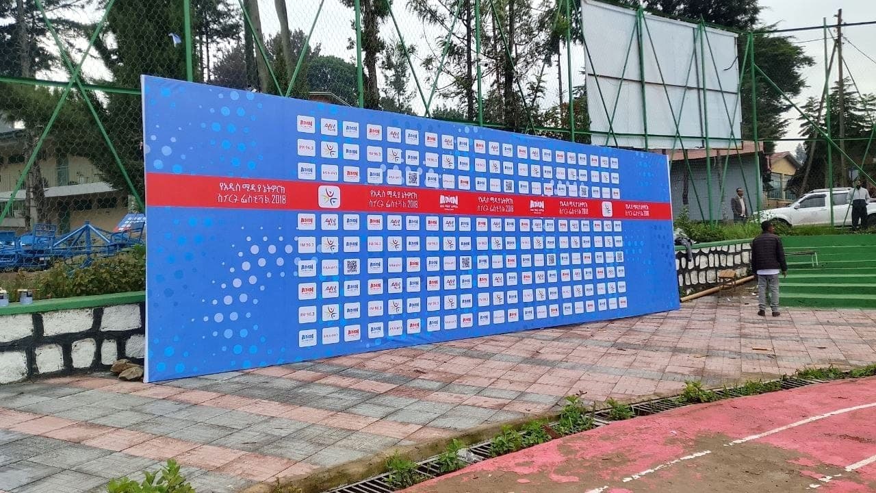 Very wide blue step-and-repeat wall for the Addis Media Network Star Festival, tiled with sponsor logos and QR codes, standing on a sports court