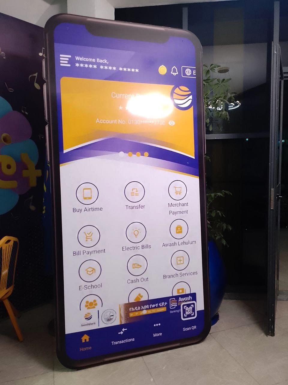 Life-size contour-cut display shaped like a smartphone showing the Awash Bank mobile banking app screen