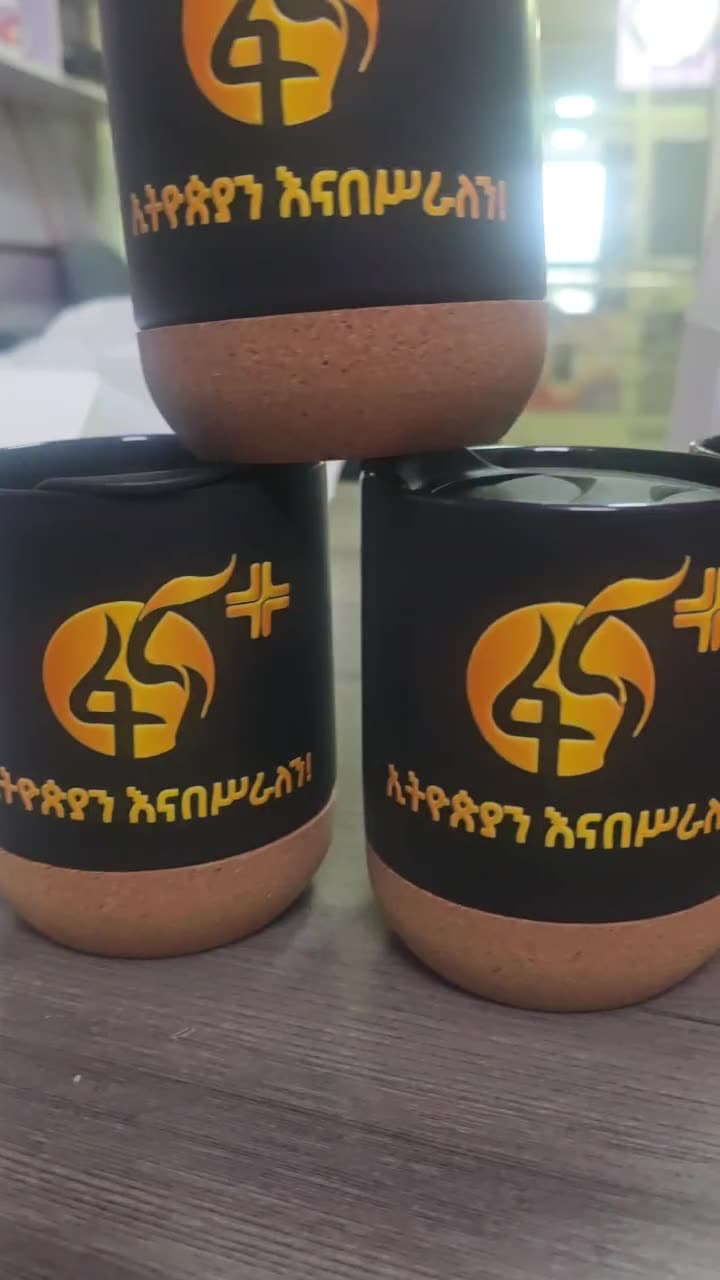 Stacked matte black travel mugs with cork bases, printed with the gold Fana 45 anniversary logo