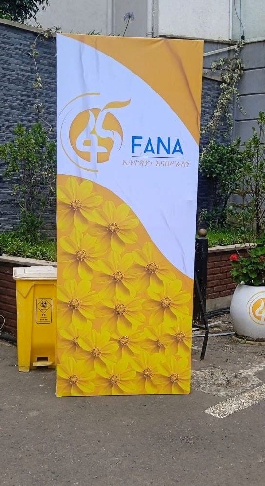 Yellow and white Fana 45 feather flag printed with meskel flowers, standing on a paved forecourt