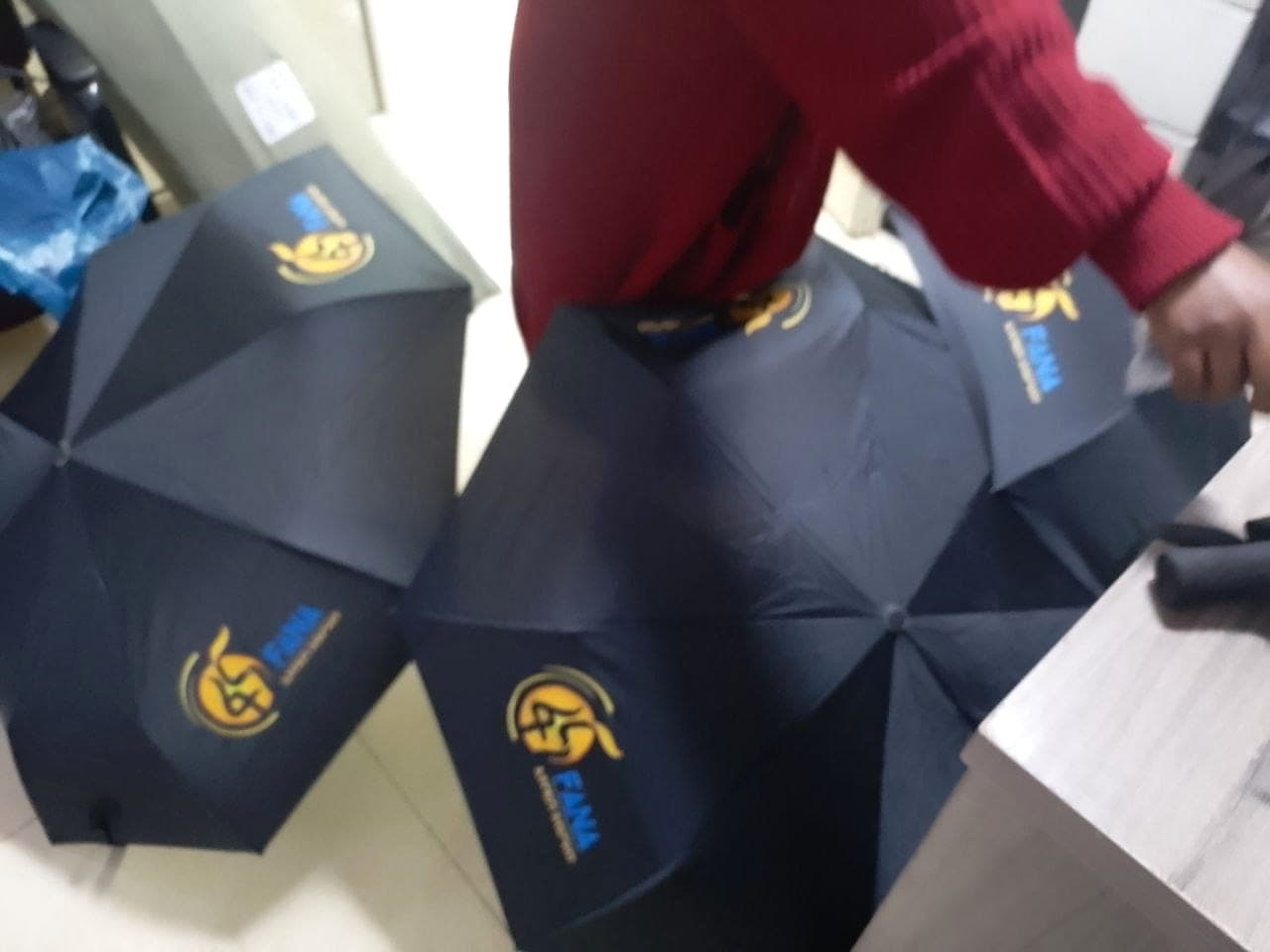 Several navy folding umbrellas printed with the gold Fana 45 anniversary mark, opened out across an office floor