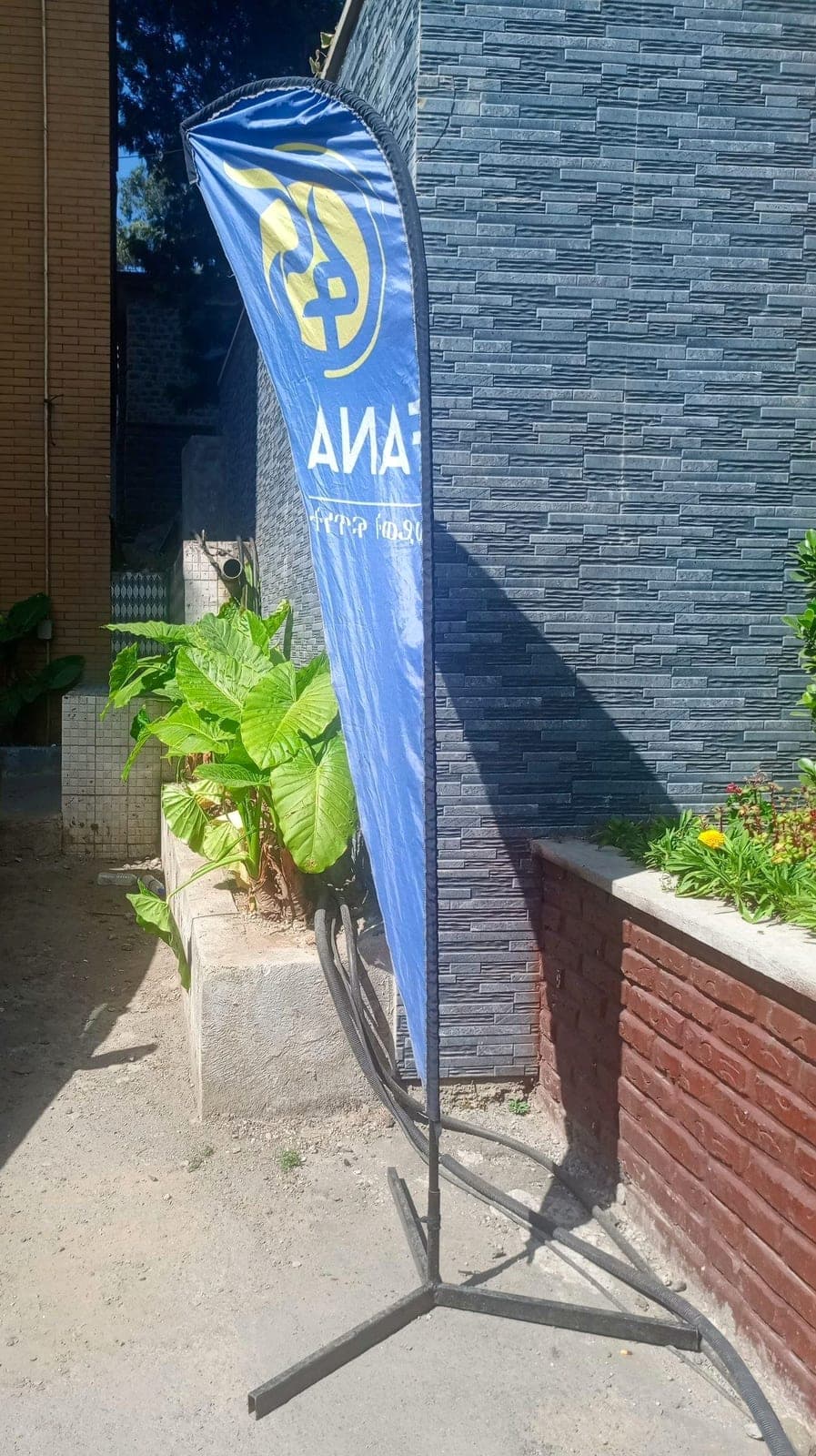Blue Fana feather flag on a weighted cross base outside a building