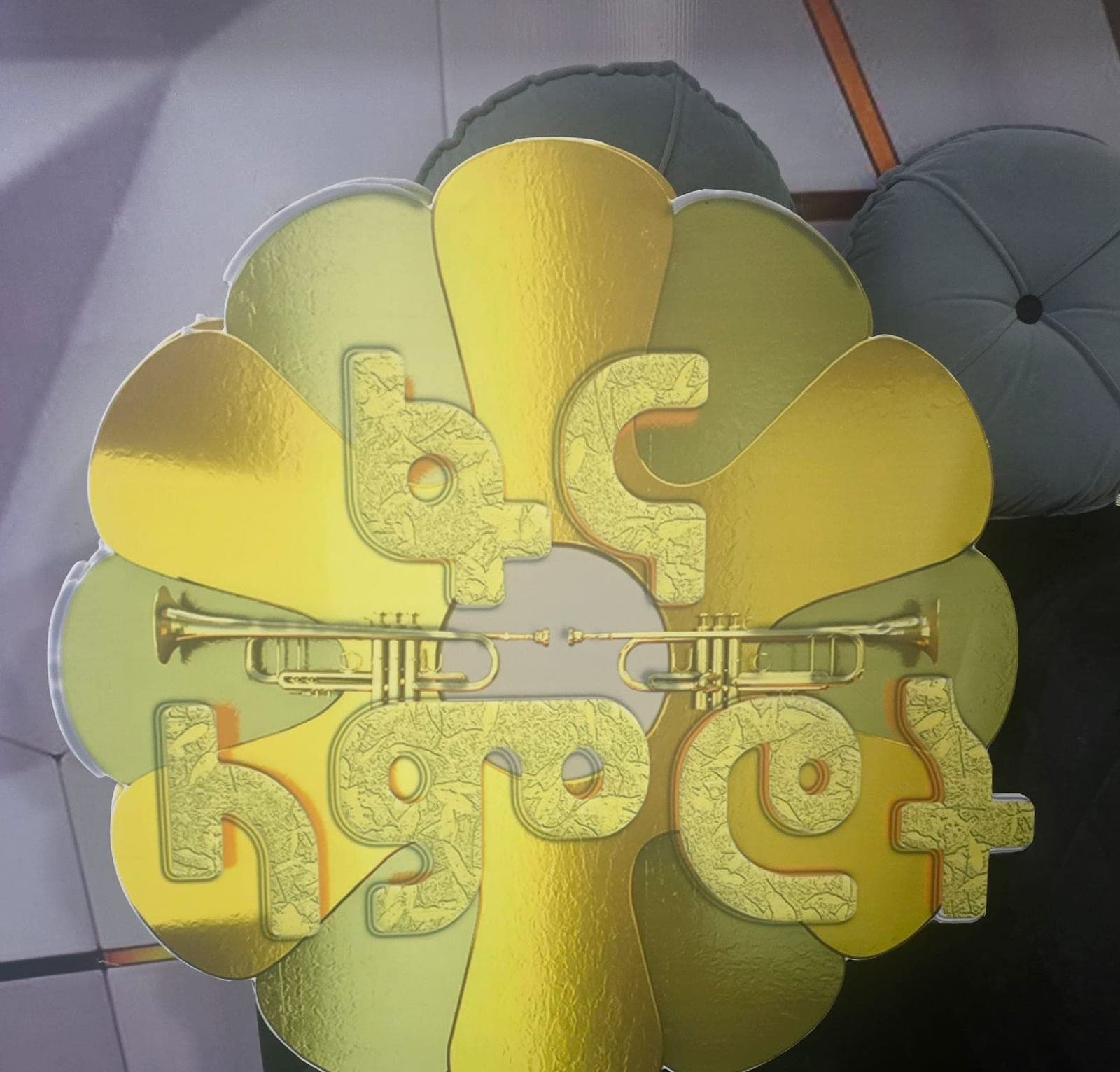 Contour-cut gold flower prop with Amharic lettering and crossed trumpets, propped against a wall before an event