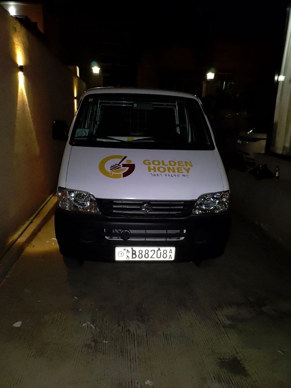 Front of a white Golden Honey van at night with the logo and Amharic strapline applied across the bonnet