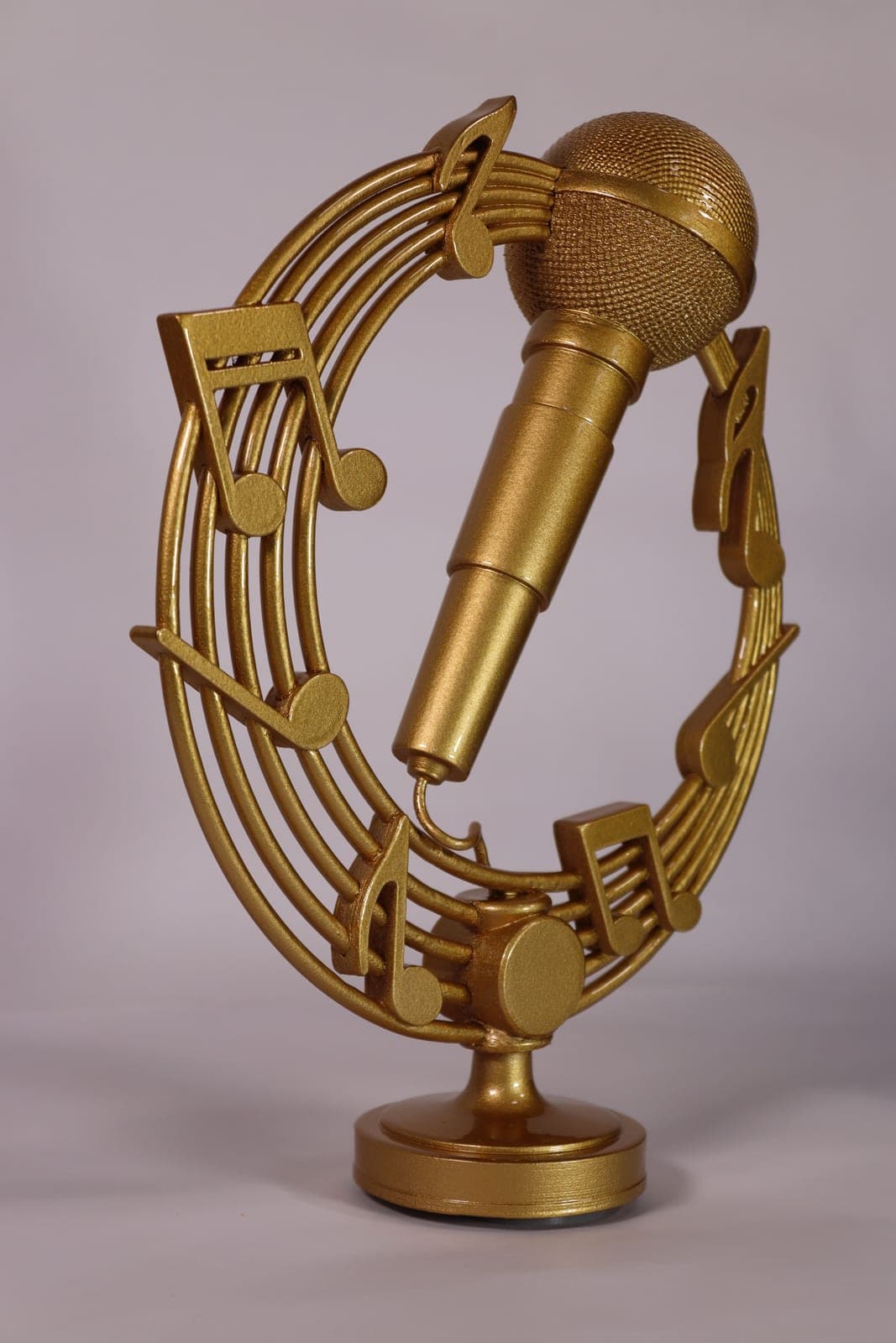 Gold trophy of a microphone set inside a curved stave of musical notes, on a turned circular base