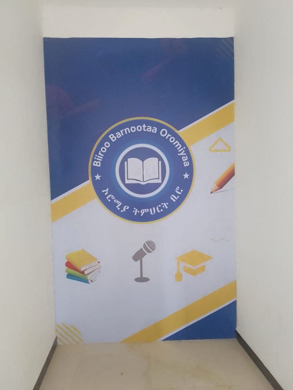 Blue and yellow Oromia Education Bureau roll-up banner printed with books, a microphone and a graduation cap