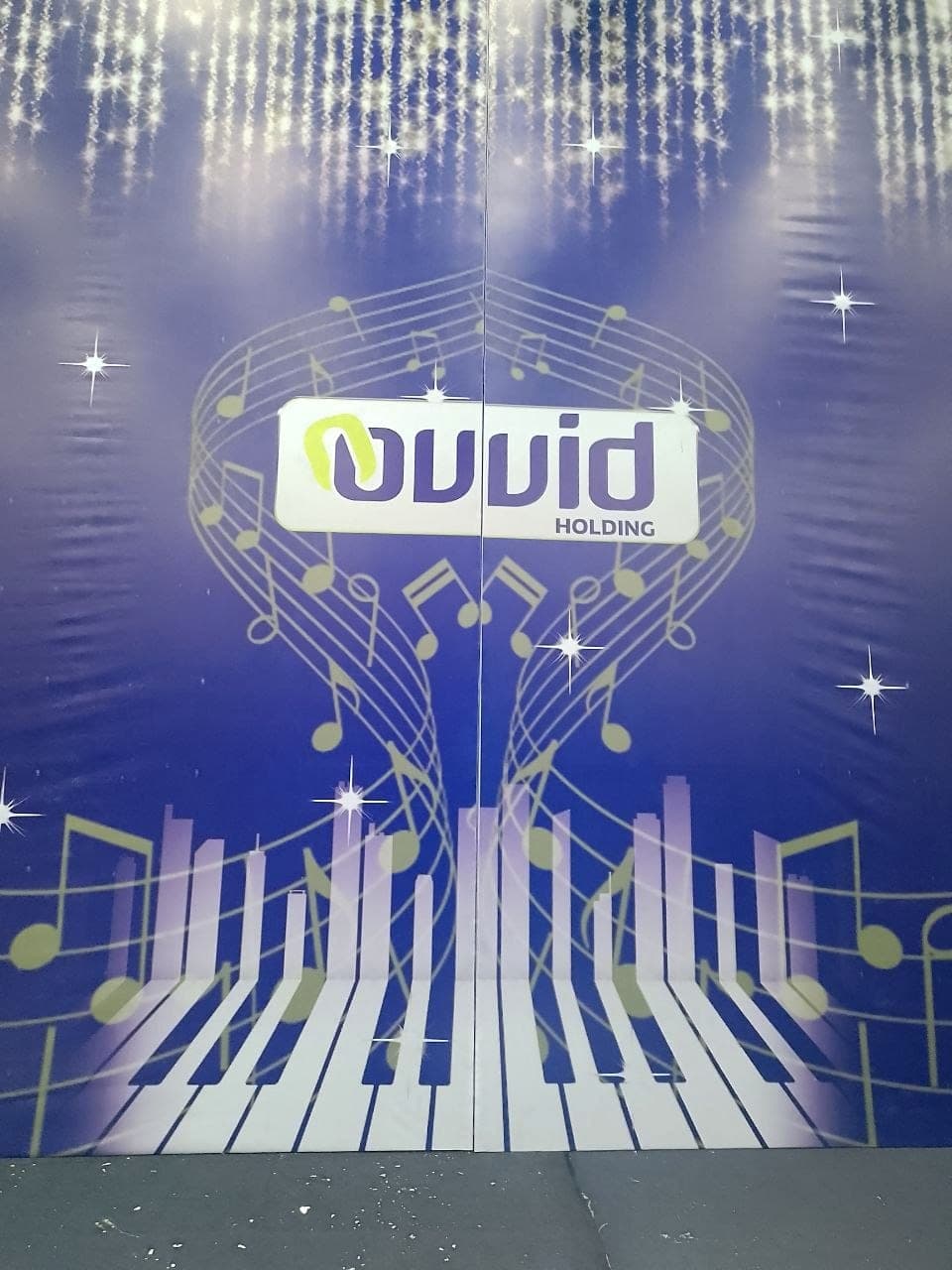 Centre panel of the Ovid Holding stage set, the logo framed by a gold stave of musical notes above printed piano keys