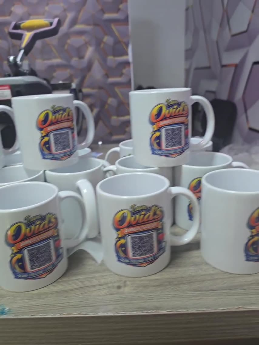 Ceramic mugs printed with Ovid's ambassador artwork, beside the heat press used to produce them