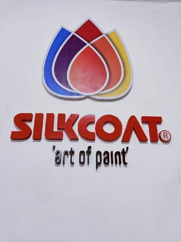 Raised red Silkcoat lettering under a three-petal paint-drop logo in blue, red and yellow, on a white wall