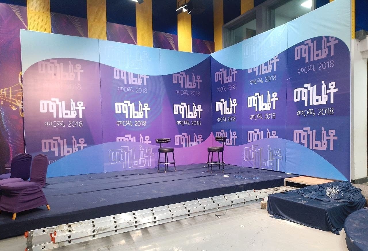 Purple and blue printed stage backdrop with two stools set for a television talk show