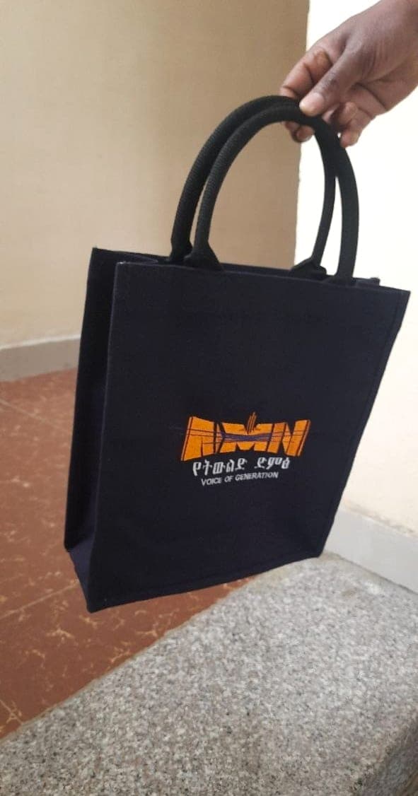 Navy canvas tote bag with rope handles, printed with the orange Addis Media Network logo and Voice of Generation line