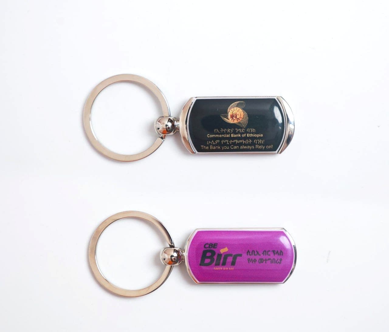 Two chrome keyrings on white, one printed with the Commercial Bank of Ethiopia mark and one with the magenta CBE Birr logo