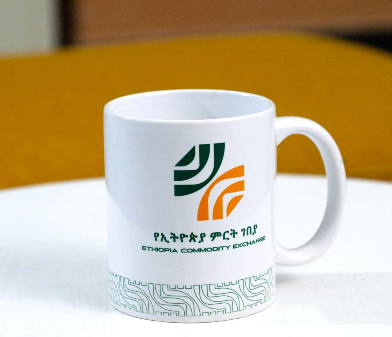White mug printed with the green and orange Ethiopia Commodity Exchange logo above a fine patterned border