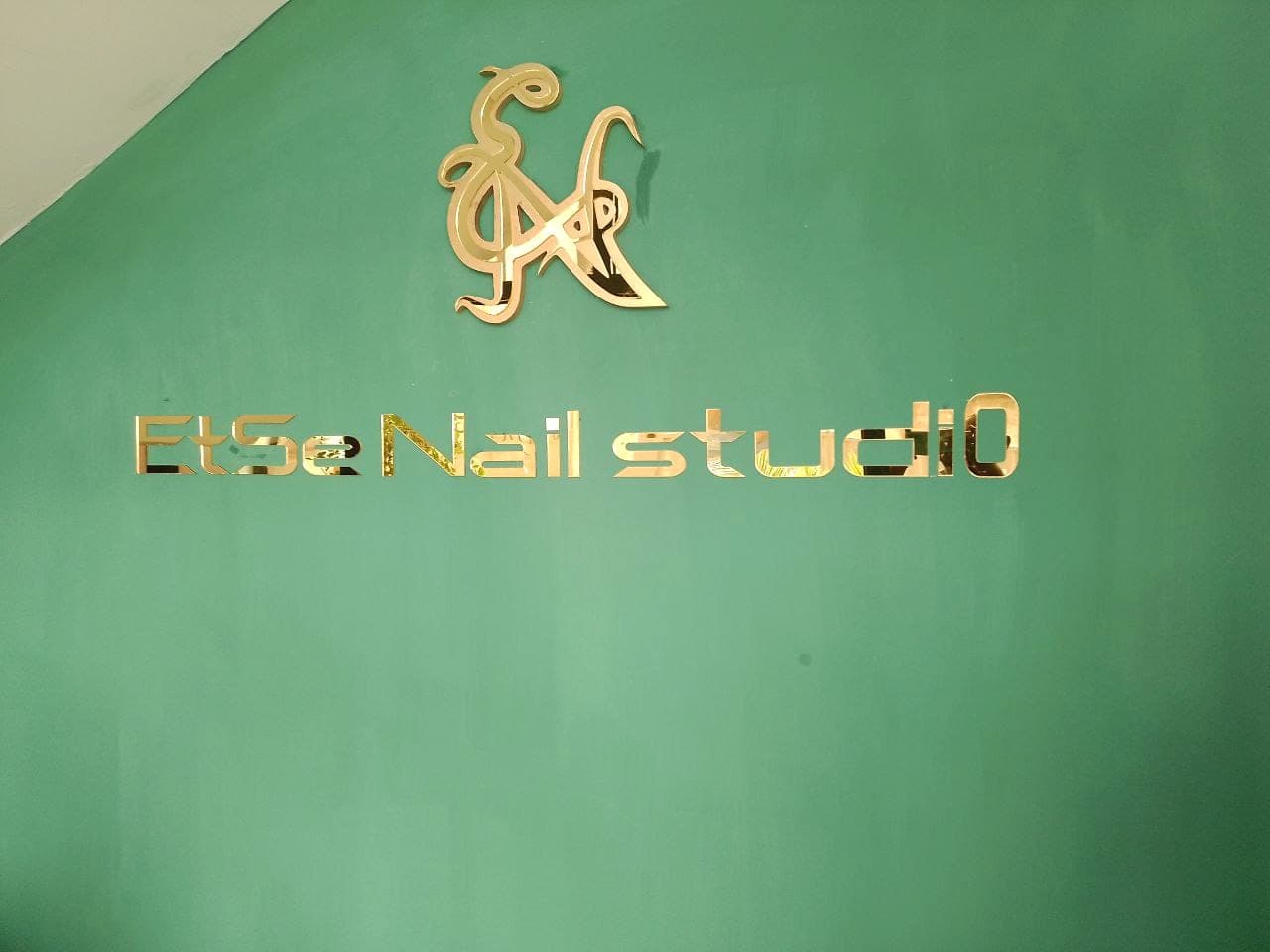 Polished gold dimensional letters reading Etse Nail Studio, with a gold monogram above, mounted on a deep green wall