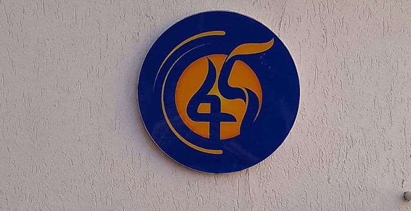 Circular blue and gold Fana 45 anniversary disc mounted on an exterior rendered wall