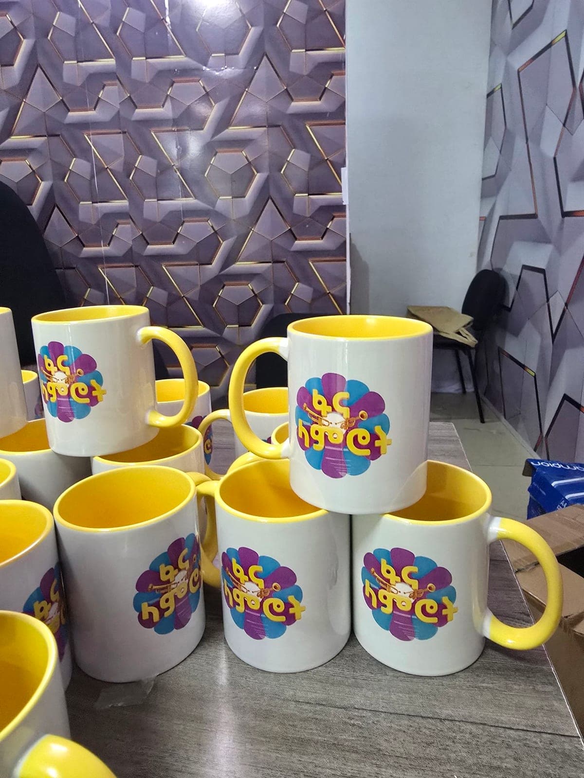 Stack of yellow-lined mugs printed with the purple and blue Fana Artists Award flower mark