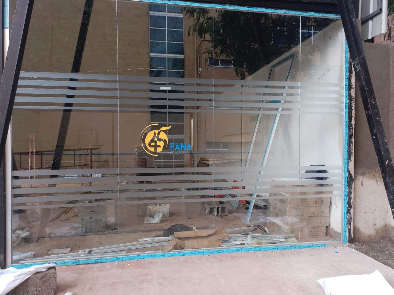 Glass shopfront with frosted vinyl banding and the gold Fana 45 logo applied, photographed during fit-out