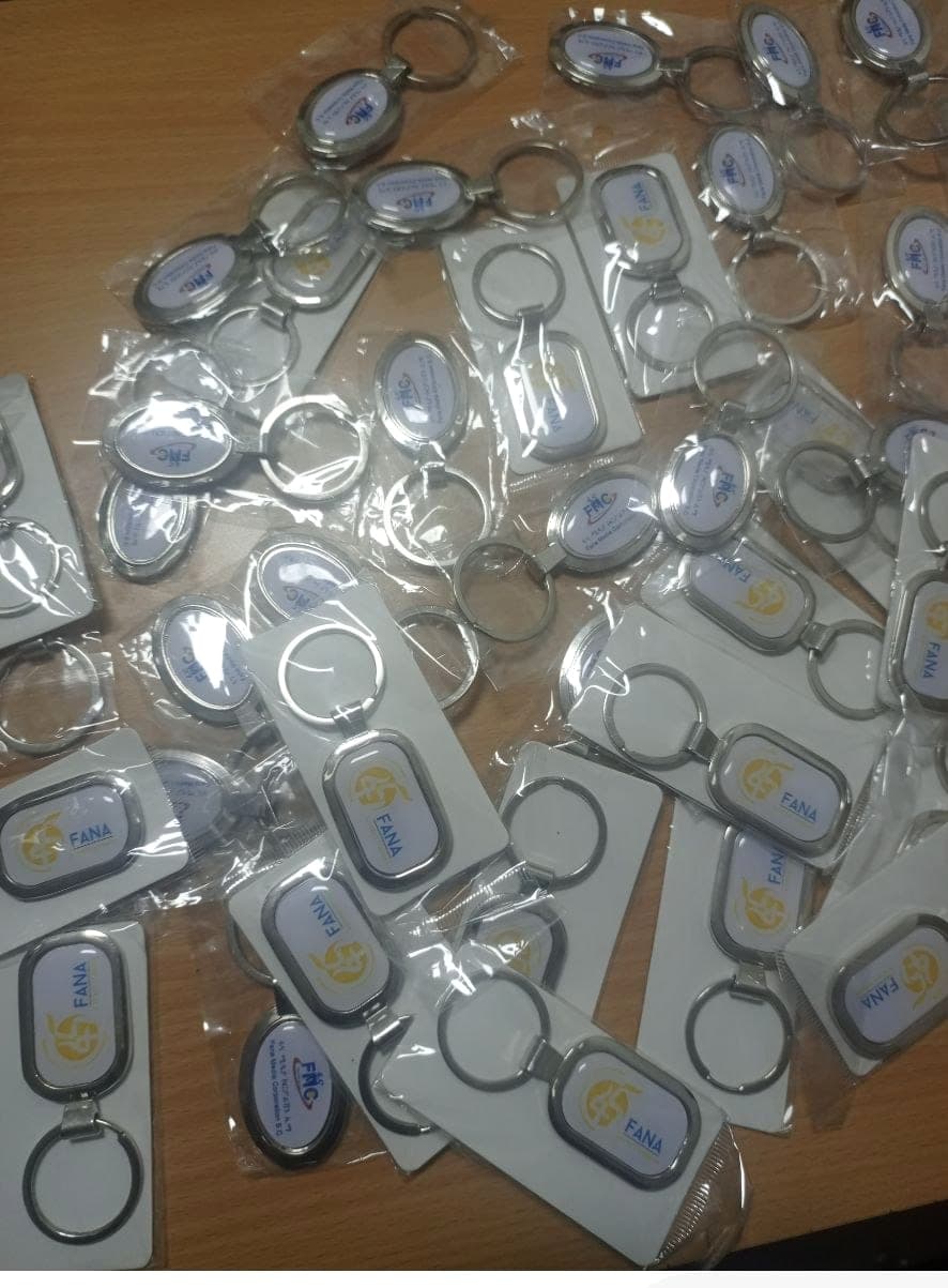 Dozens of individually bagged metal keyrings printed with the Fana and FMC logos, spread across a desk
