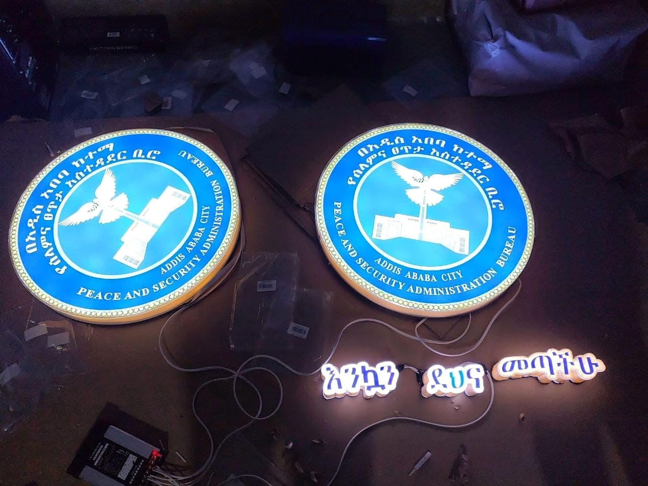 Two large illuminated blue crest signs for the Addis Ababa City Peace and Security Administration Bureau lit up in the workshop alongside glowing Amharic letters